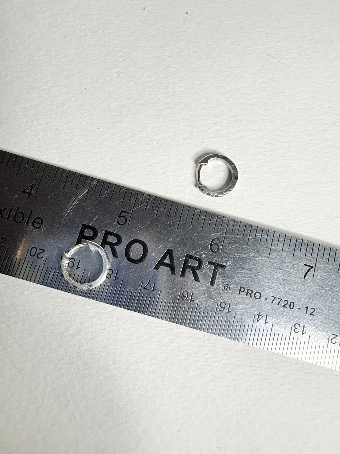 Sterling silver small huggie hoop earrings with rhodolite garnets, shown with a ruler.