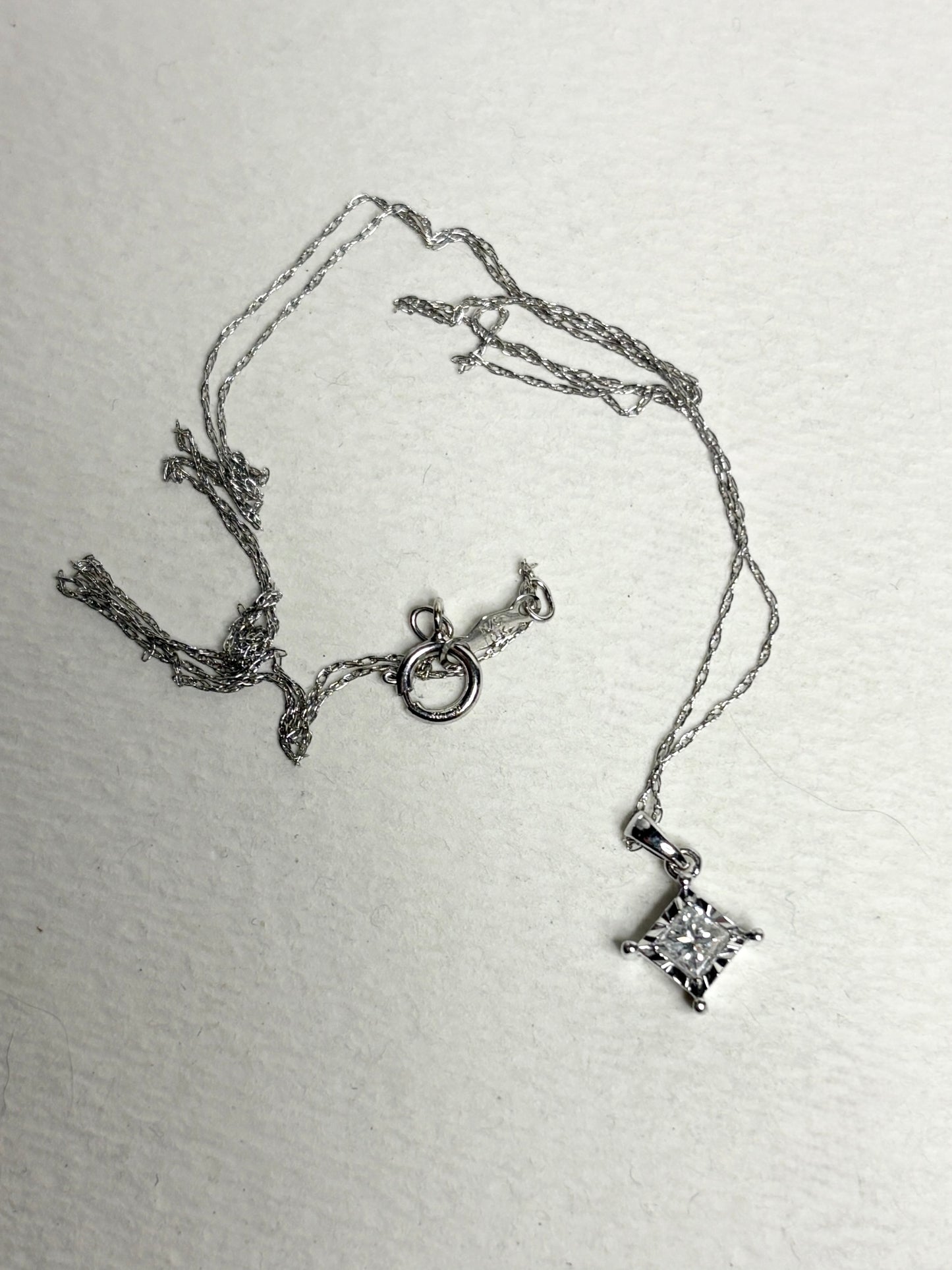 A 10k white gold pendant necklace with a princess cut diamond.