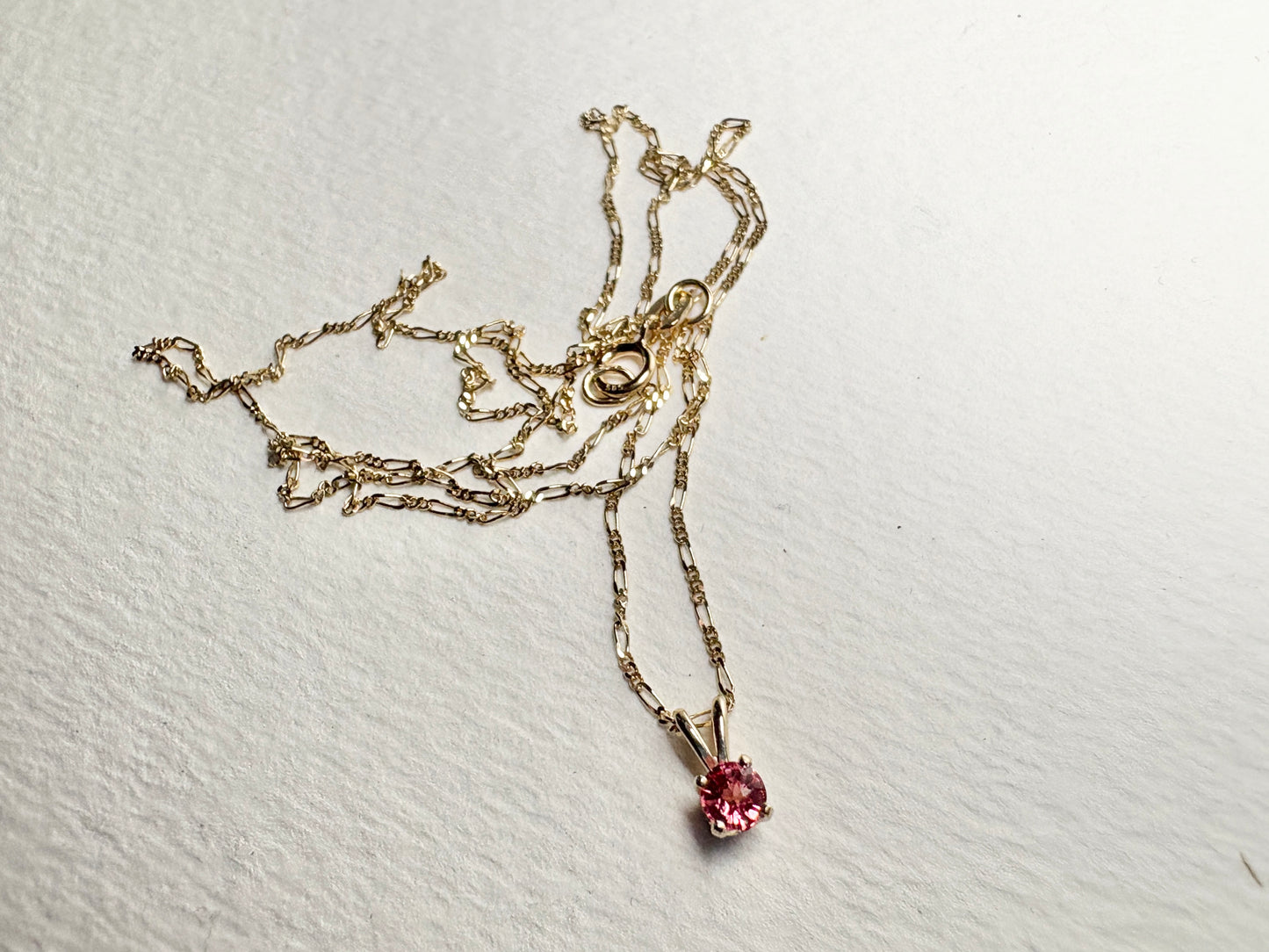 A delicate 14k gold chain holds a small, round pink sapphire pendant.