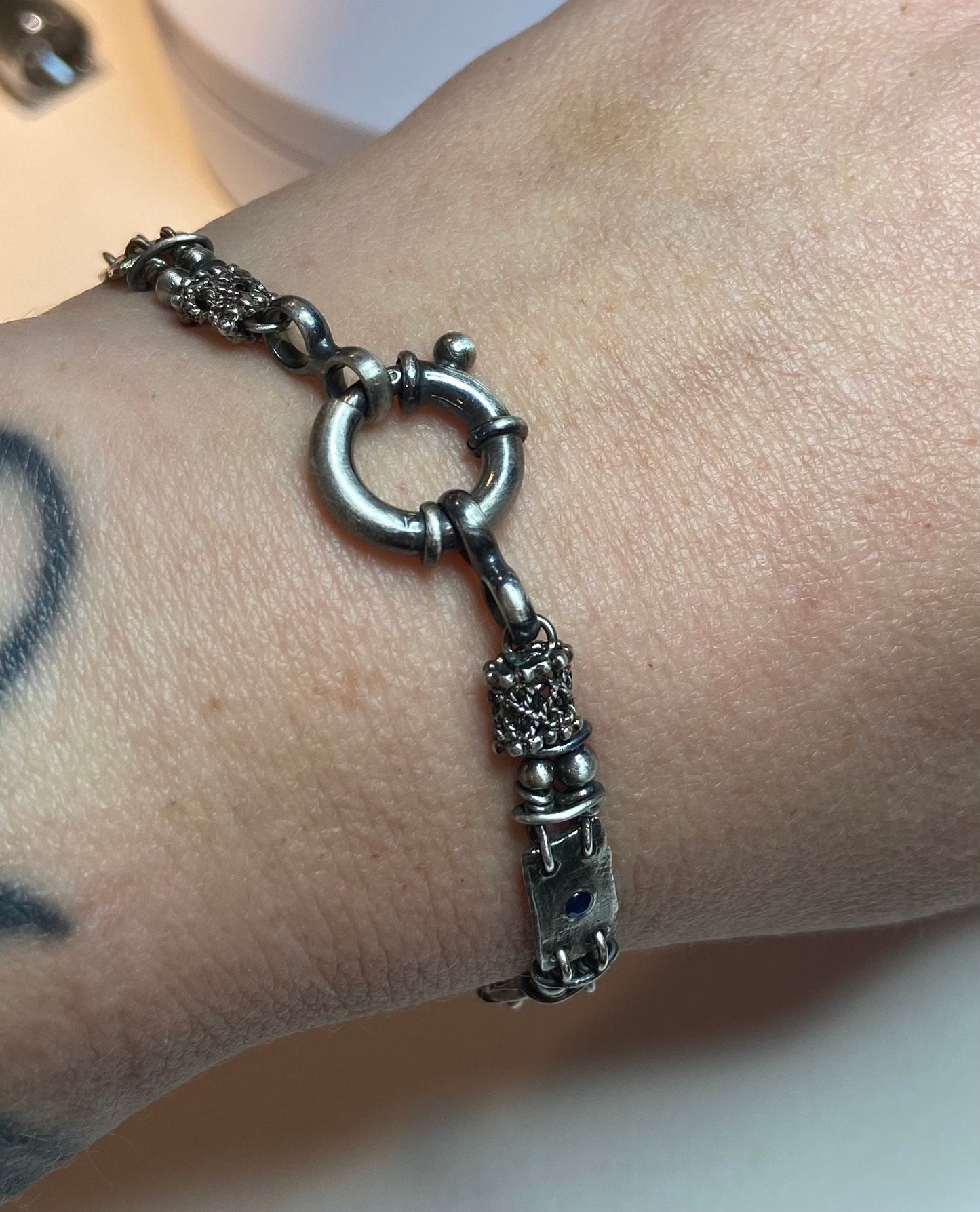 Hand-forged sterling silver bracelet with a circular clasp and a small blue sapphire accent.