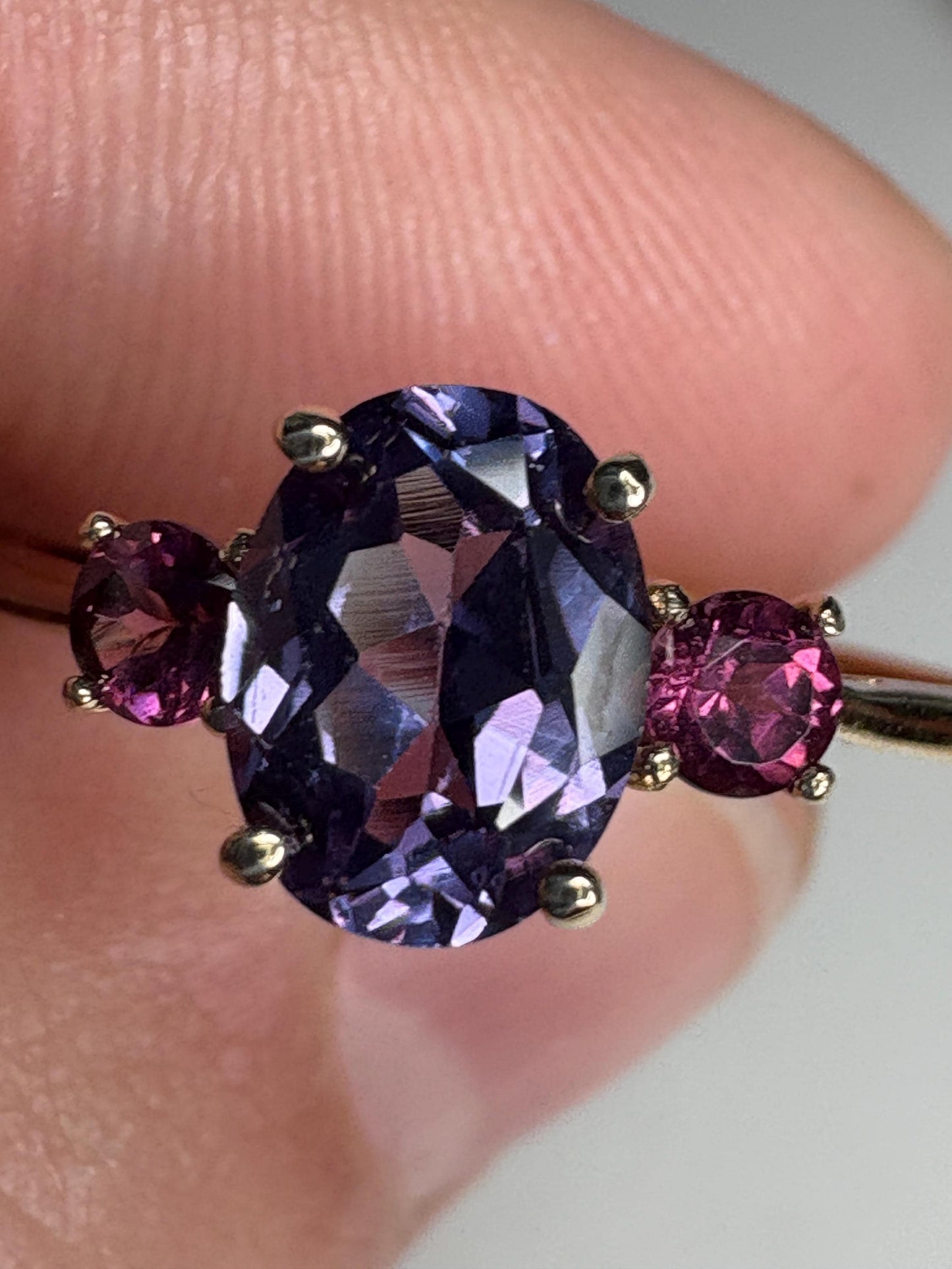 Ring with oval color change synthetic sapphire and two round umbalite garnets in gold.