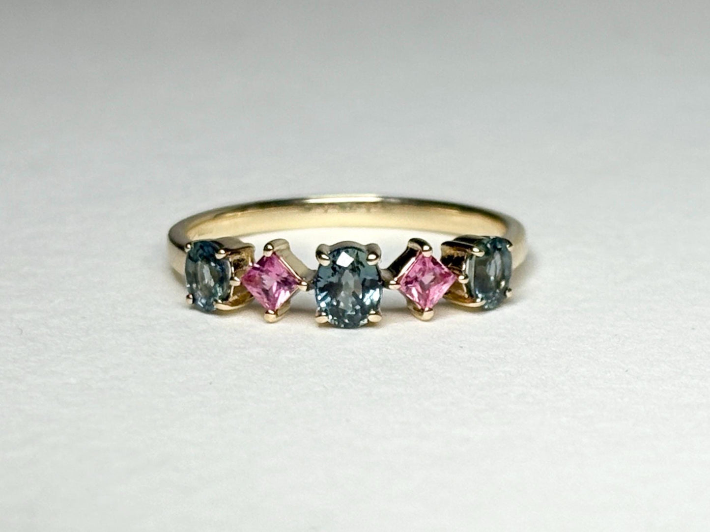 A 9k gold band ring with oval steel blue and square pink sapphires.