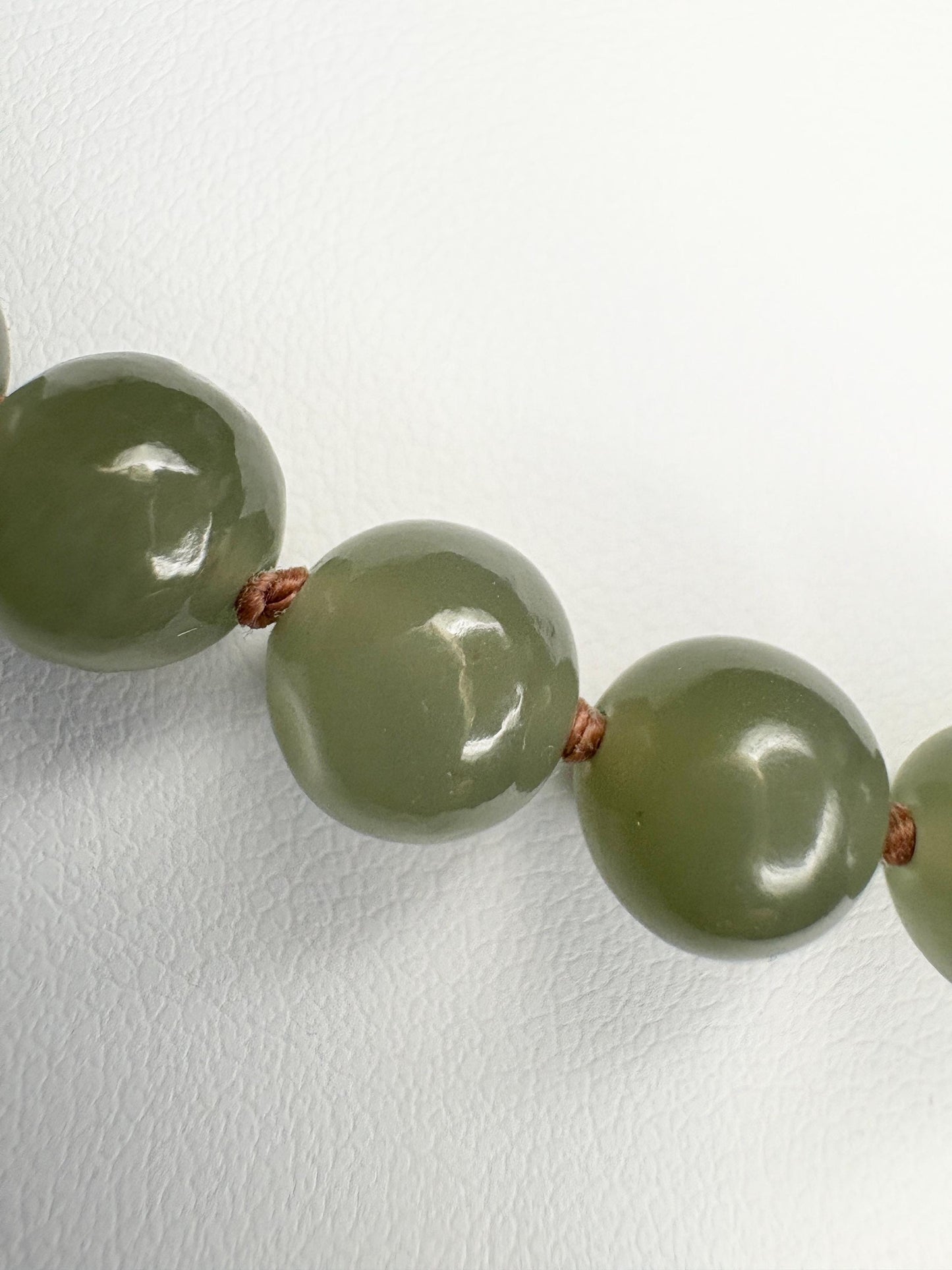 Nephrite Hetian jade beads knotted on a brown cord with a sterling silver toggle clasp.