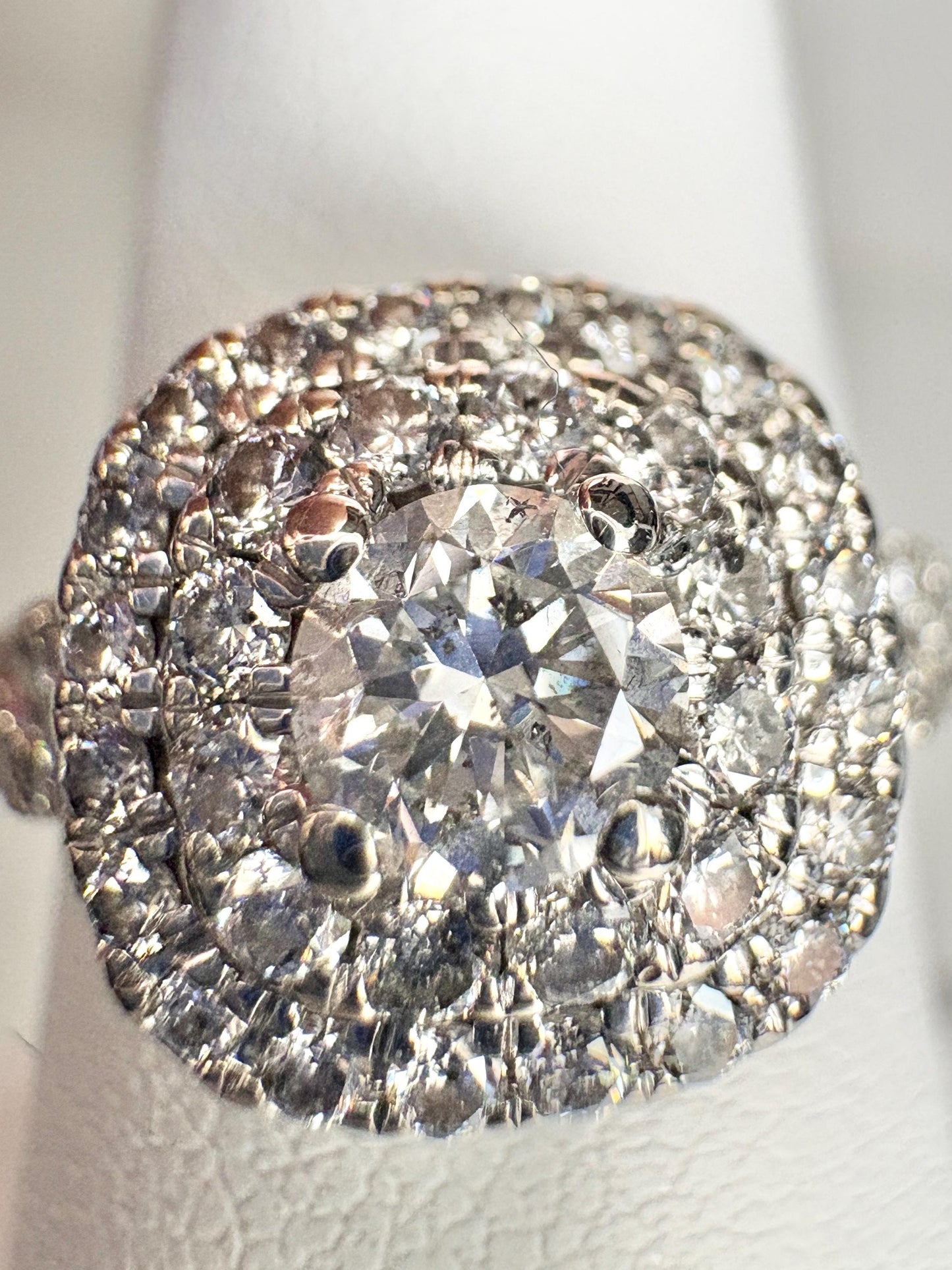 A 14k white gold ring with a central diamond surrounded by a double halo of smaller diamonds.