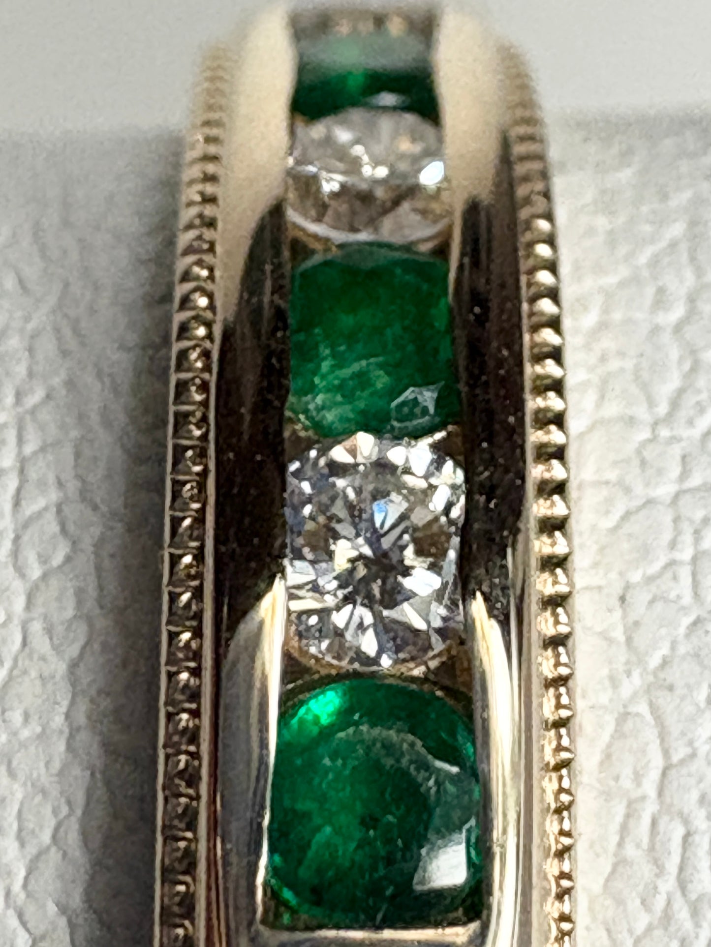 A channel-set band ring with alternating diamonds and emeralds in 18k gold.