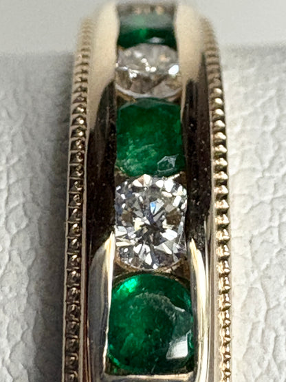 A channel-set band ring with alternating diamonds and emeralds in 18k gold.
