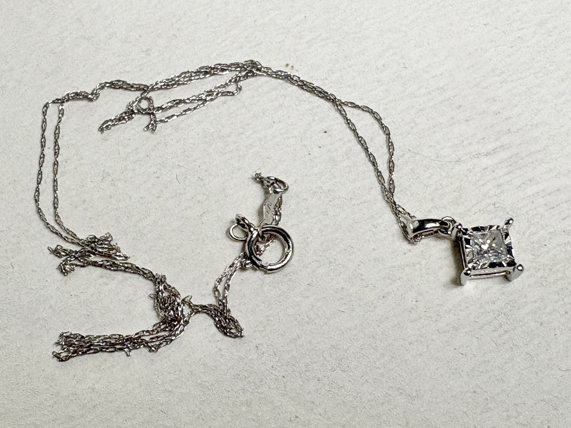 A 10k white gold pendant necklace with a princess cut diamond on a thin rope chain.