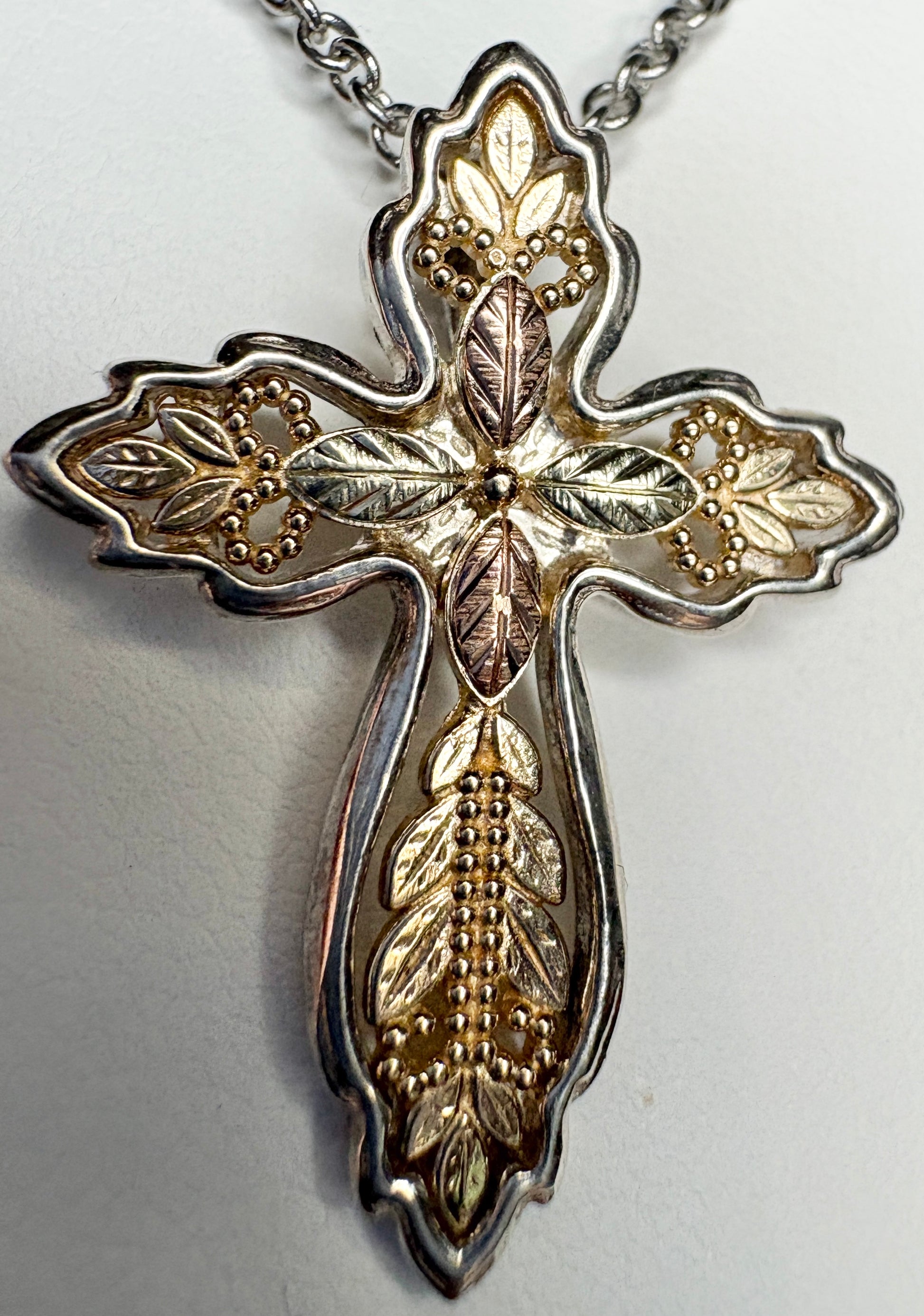 Black Hills Gold ornate cross pendant with sterling silver frame and 10k gold leaves.