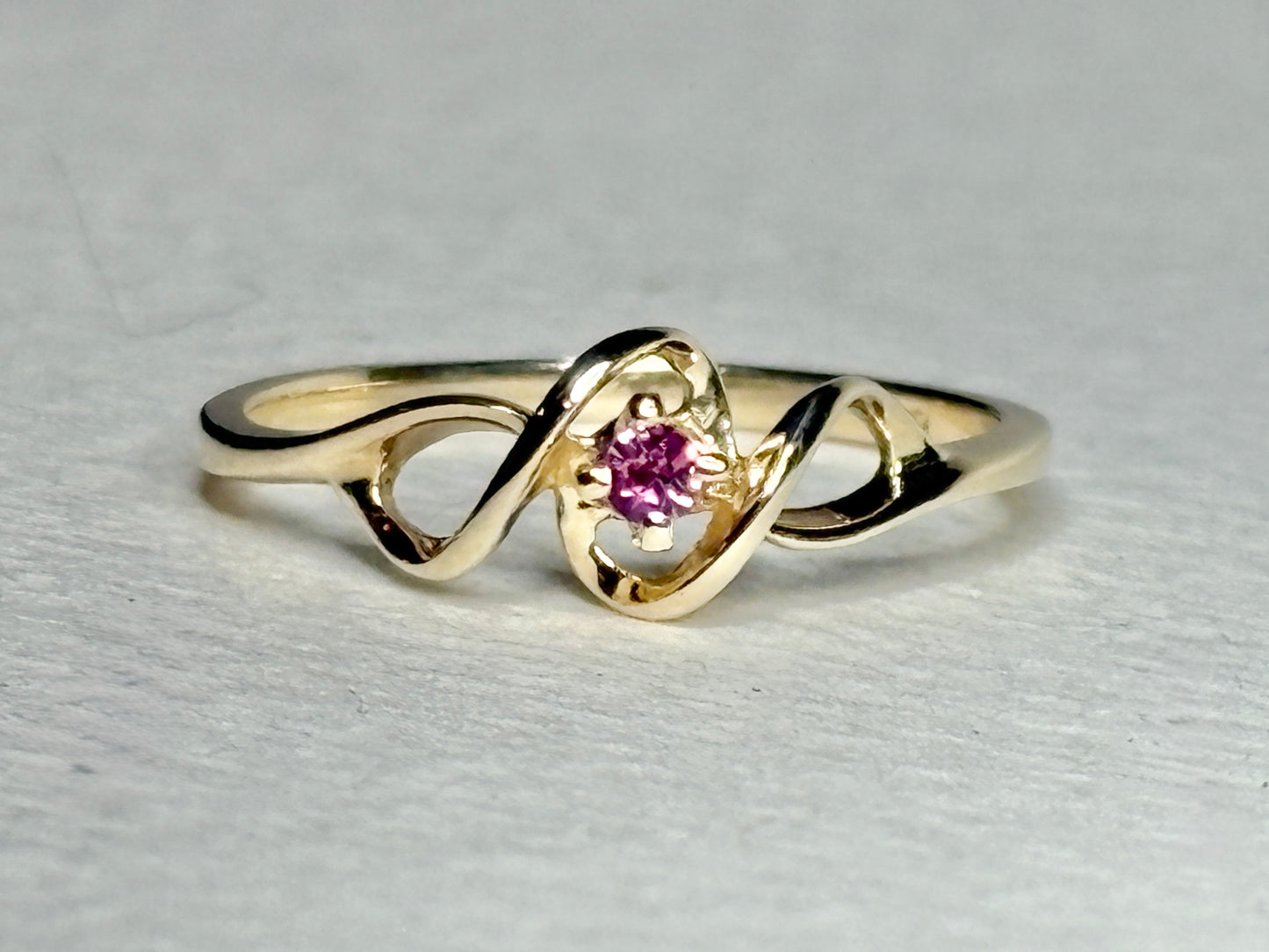 A 10k gold ribbon ring with a pink bixbite gemstone.