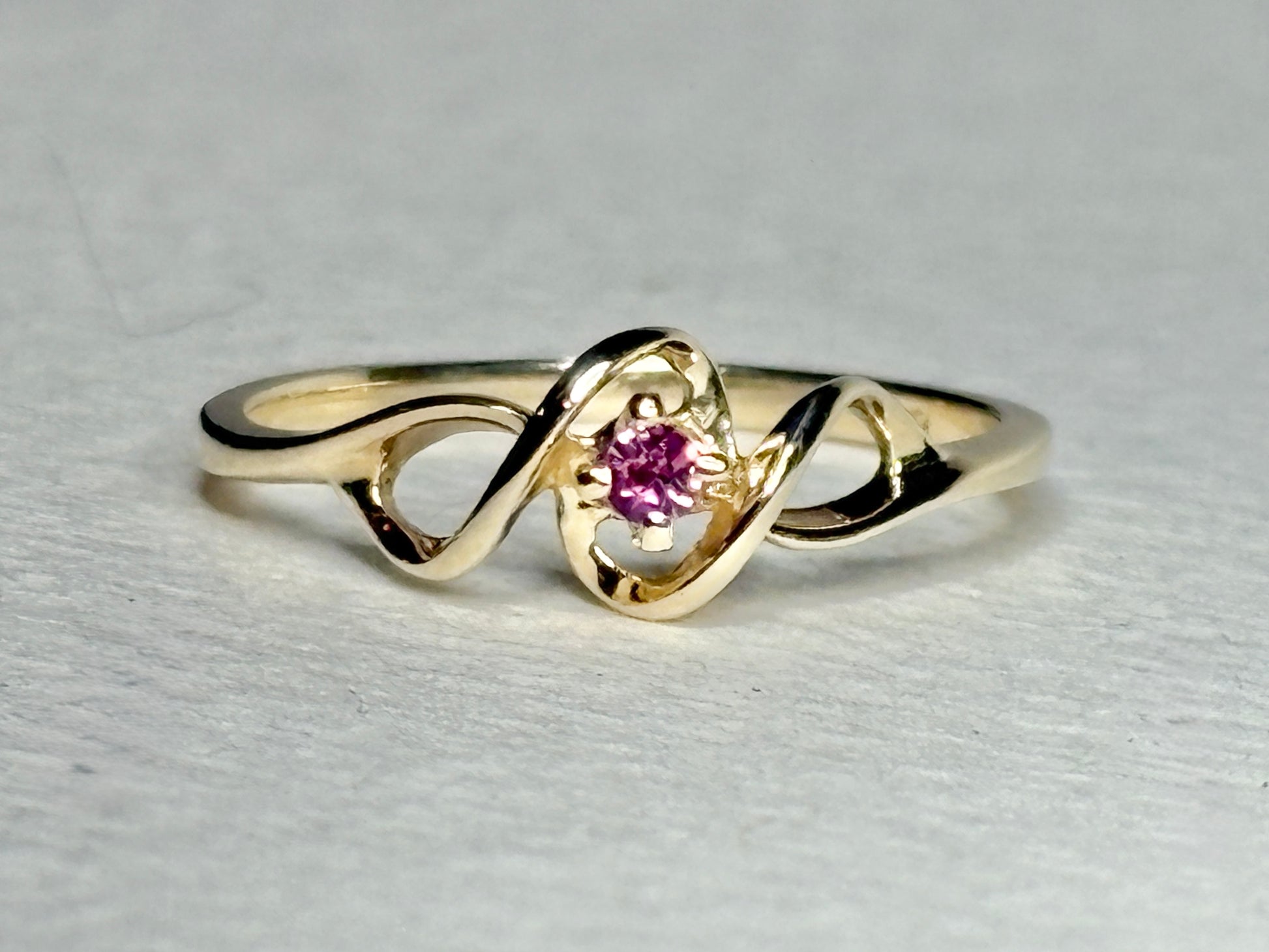 A 10k gold ribbon ring with a pink bixbite gemstone.