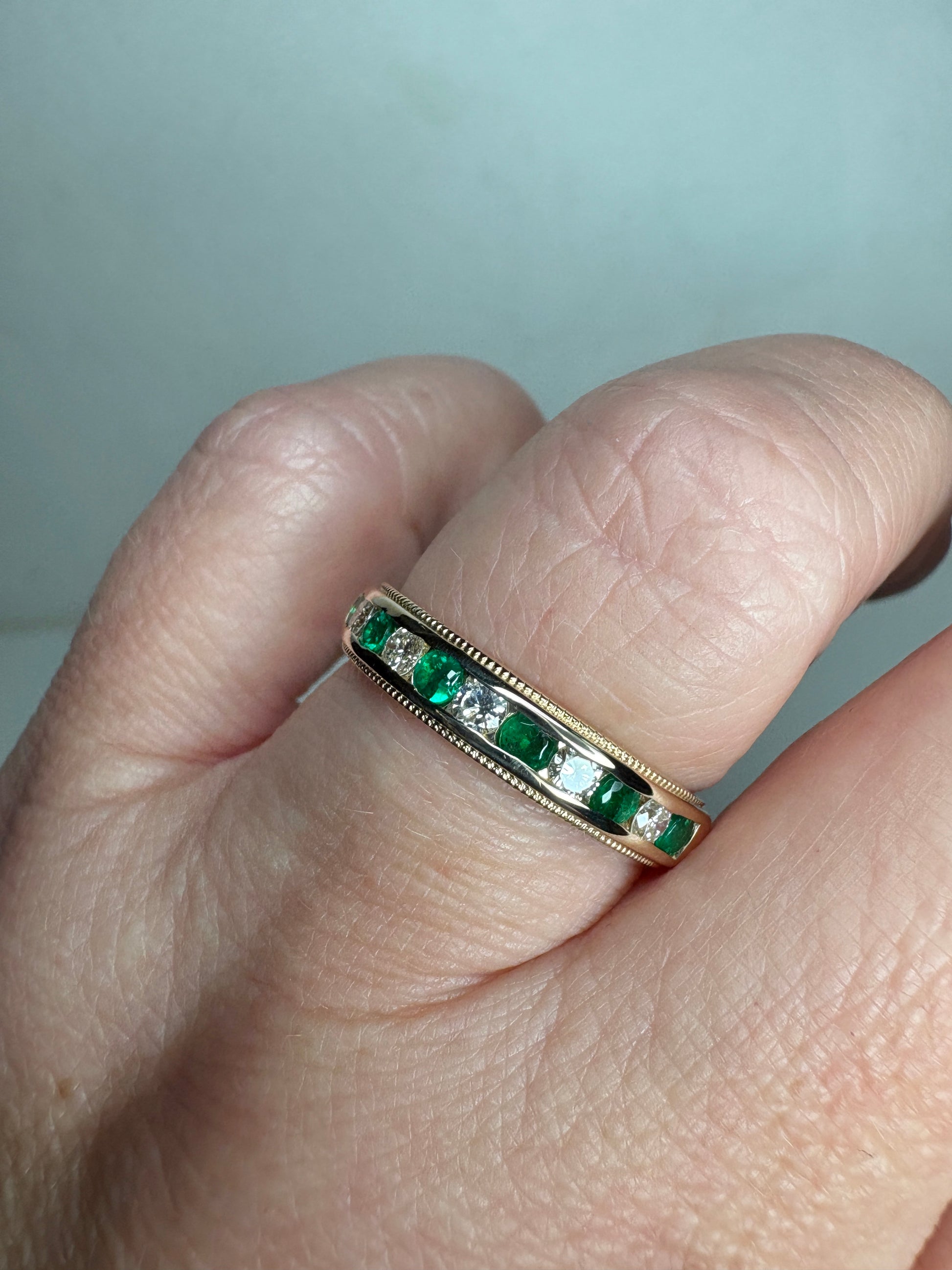 18k gold ring with alternating emeralds and diamonds in a channel setting.