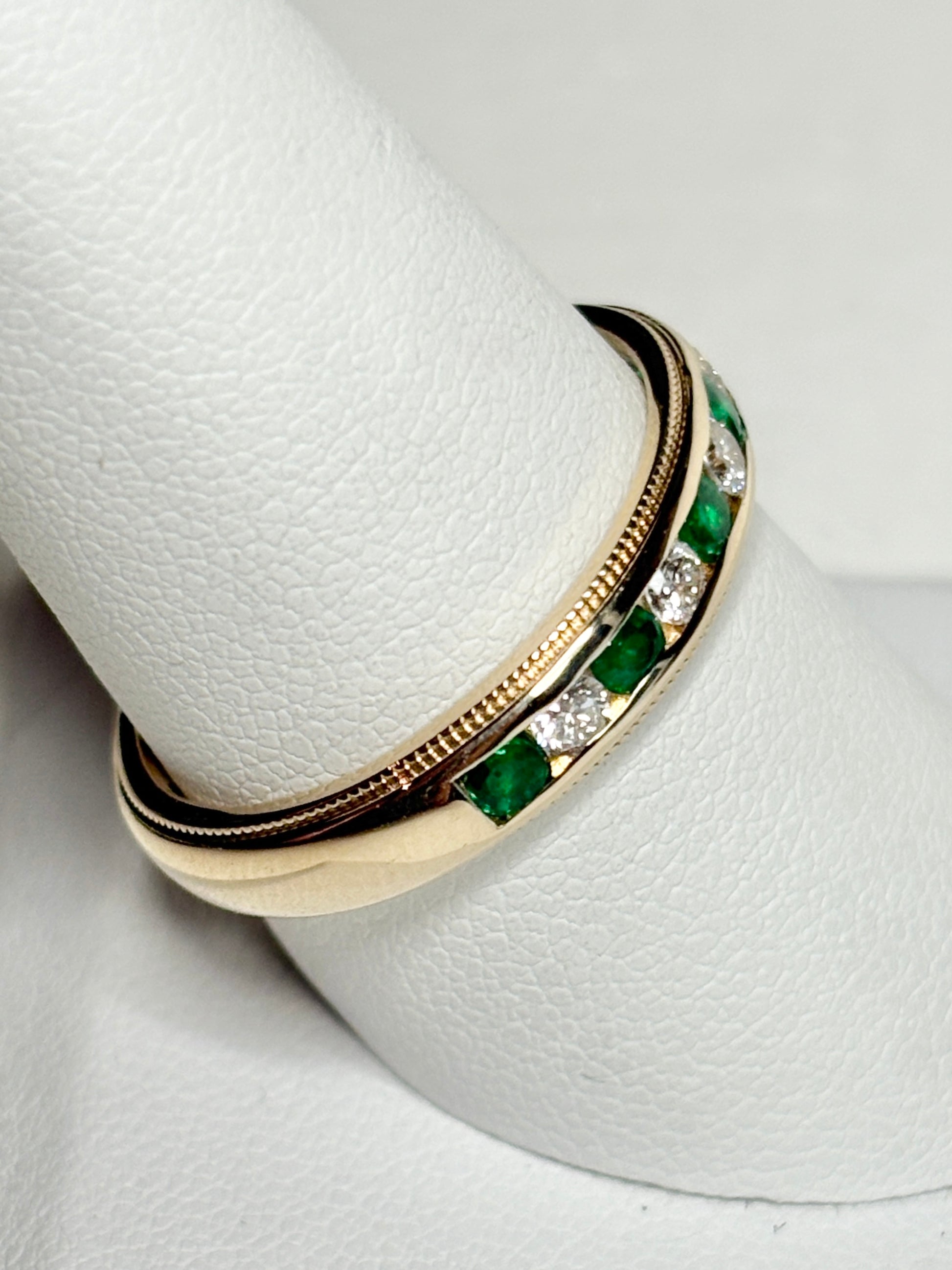 18k gold band with alternating emeralds and diamonds, featuring milgrain detailing.