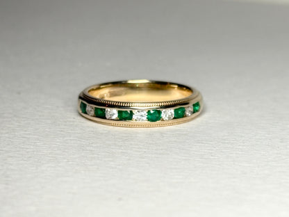 18k gold band with alternating emeralds and diamonds, featuring milgrain detailing.