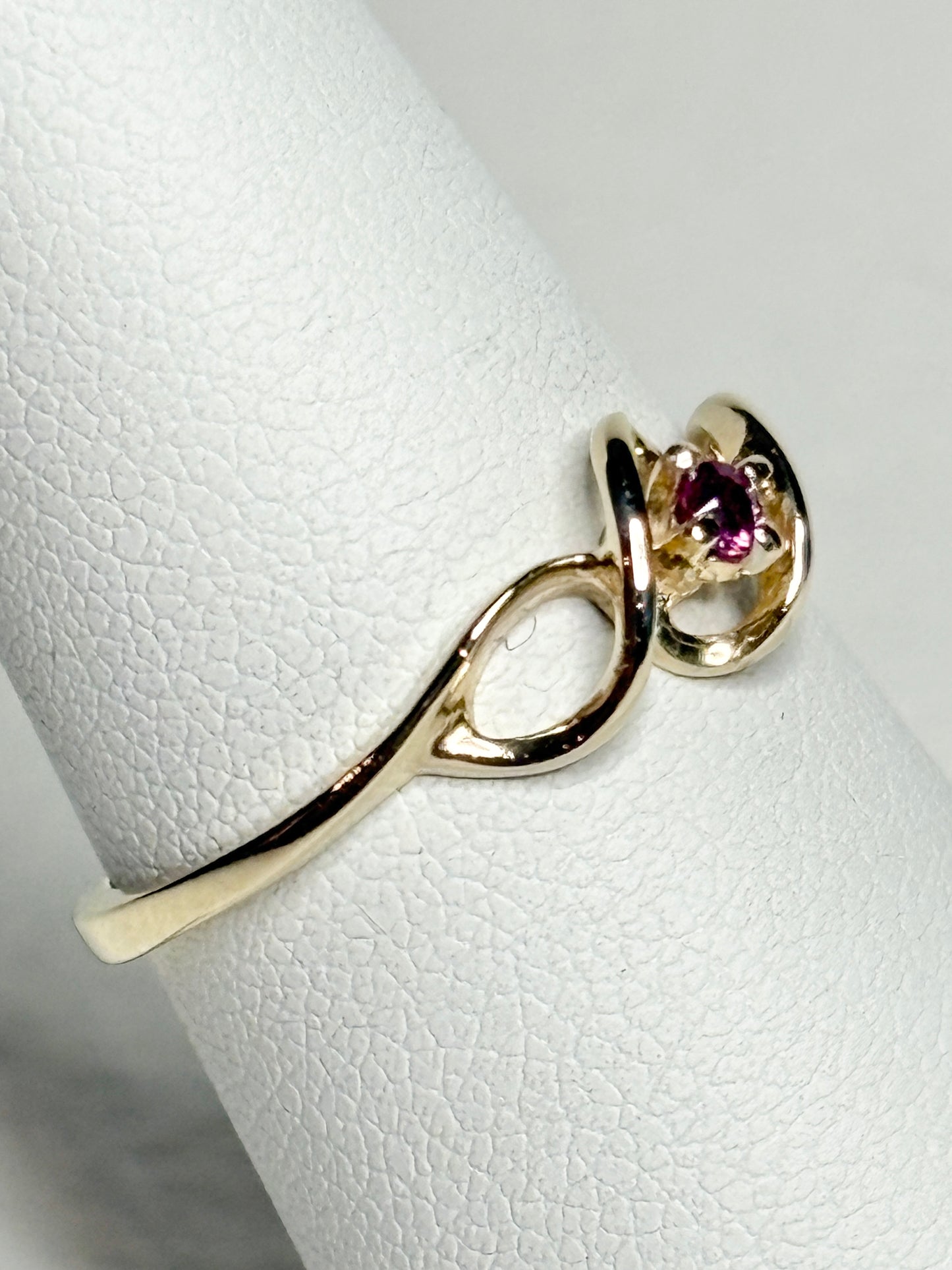 A 10k gold ribbon ring with a small pink bixbite gemstone.