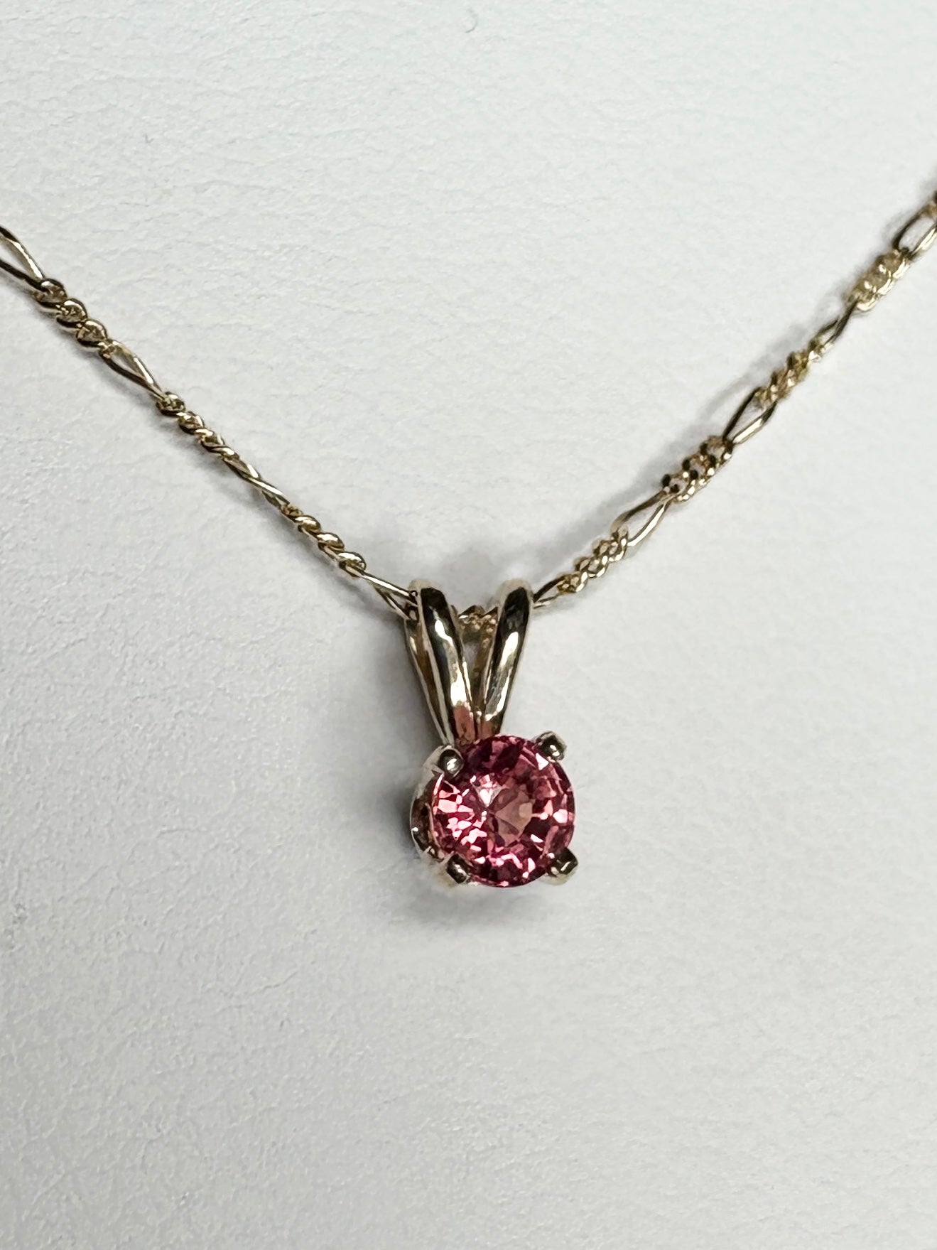 Small pink sapphire solitaire pendant necklace on a delicate gold chain.