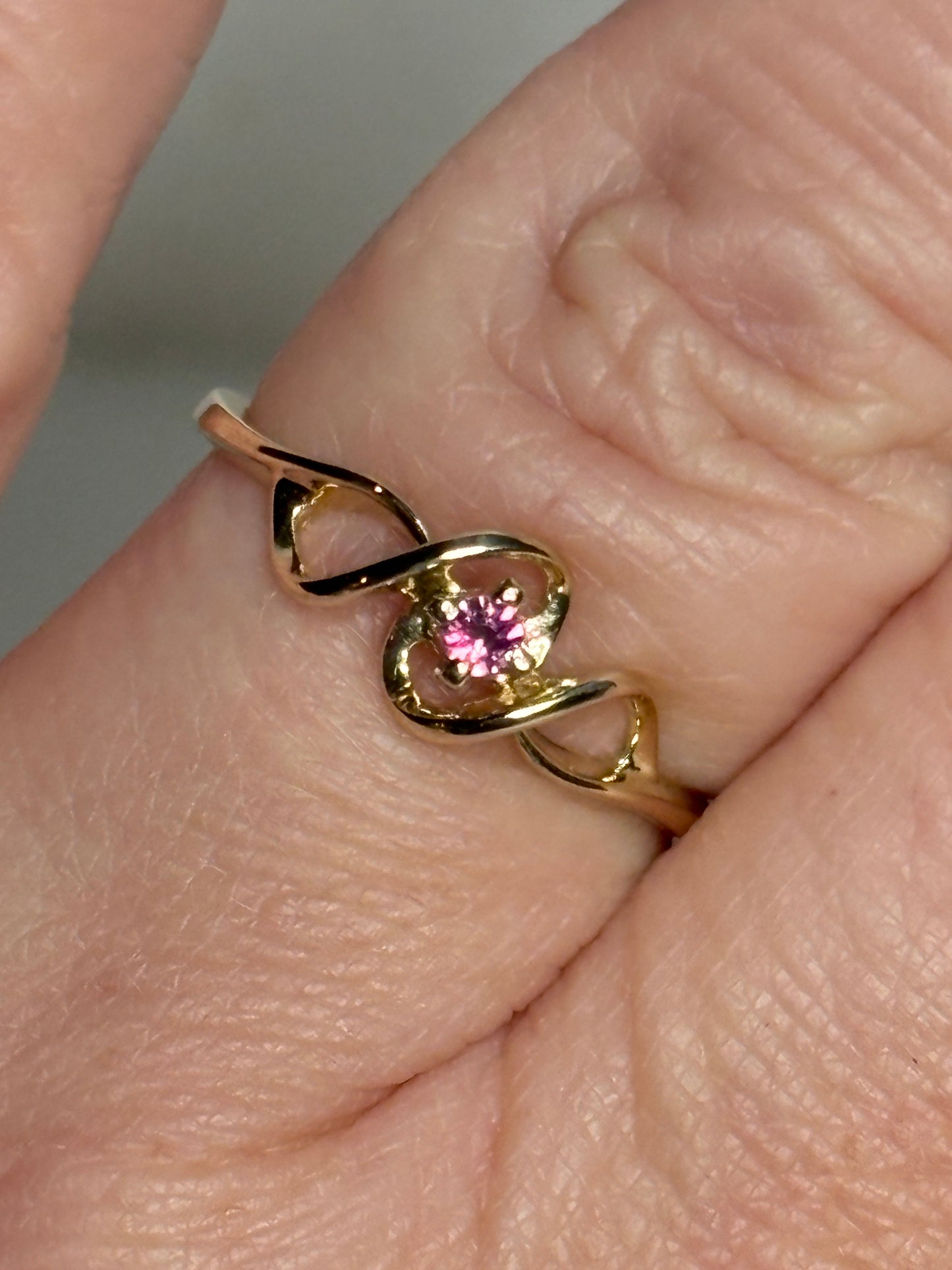 A delicate gold ribbon ring with a small pink gemstone.