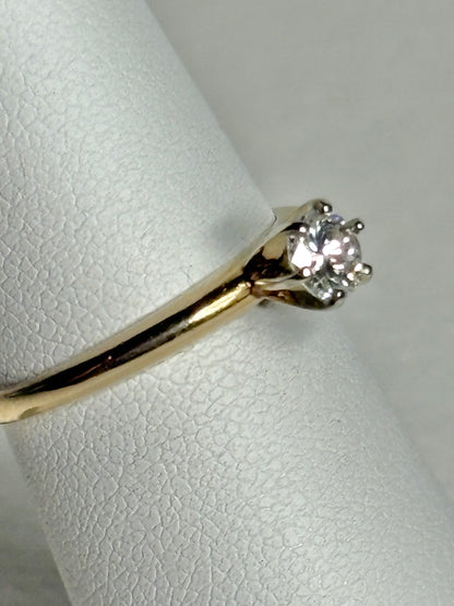 A 14k gold ring with a single diamond on a textured white surface.