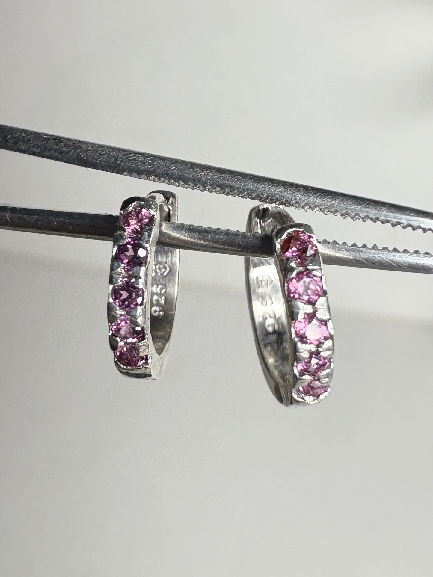 Small sterling silver huggie hoop earrings with rhodolite garnets.