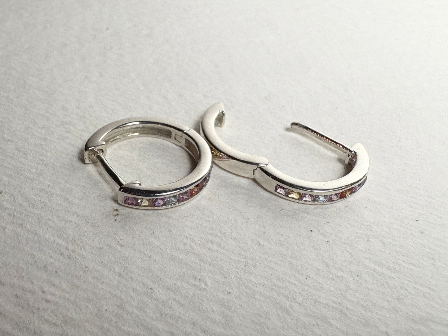 Sterling silver huggie hoop earrings with princess-cut multi-color sapphires.