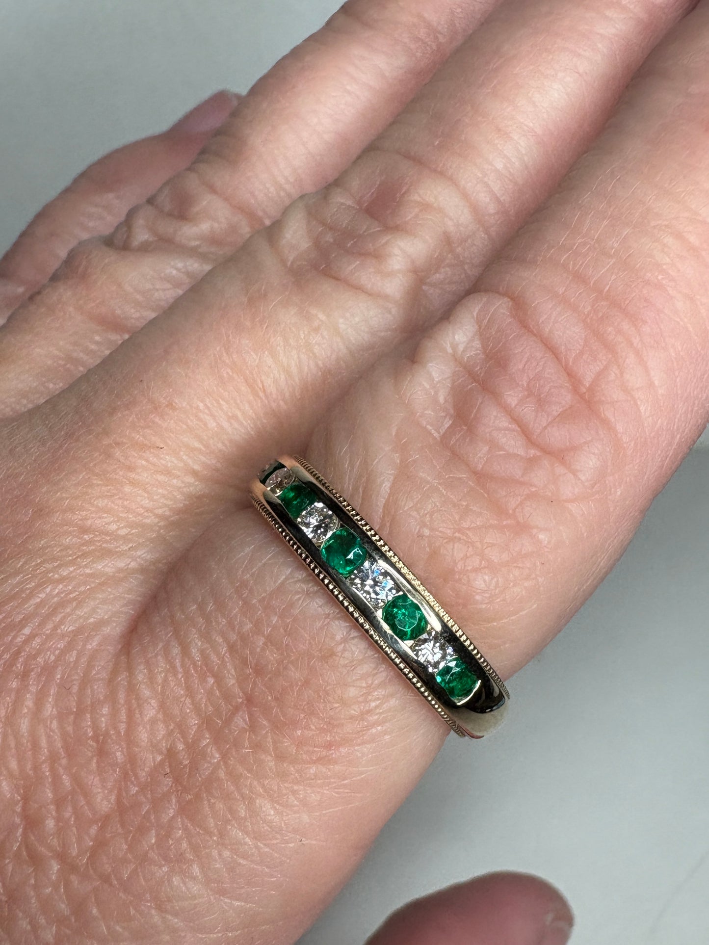 18k gold band with alternating emeralds and diamonds, featuring milgrain detailing.
