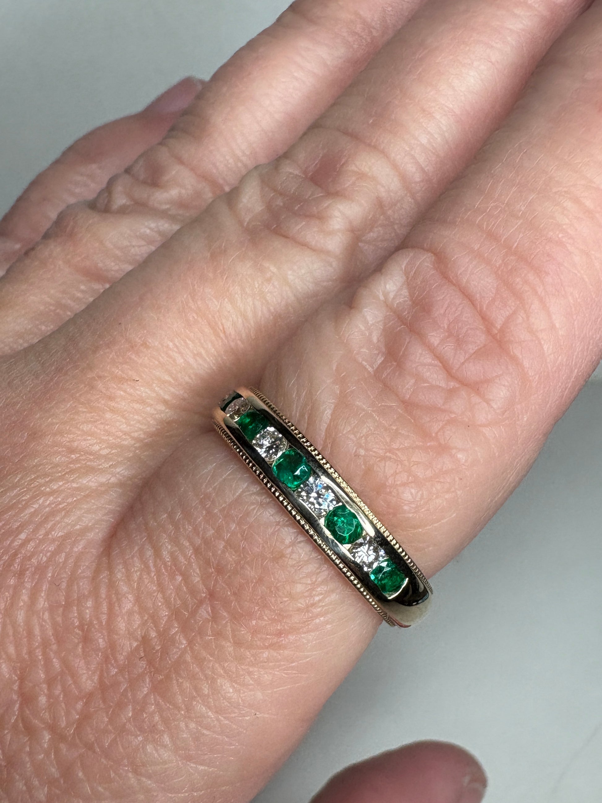 18k gold band with alternating emeralds and diamonds, featuring milgrain detailing.