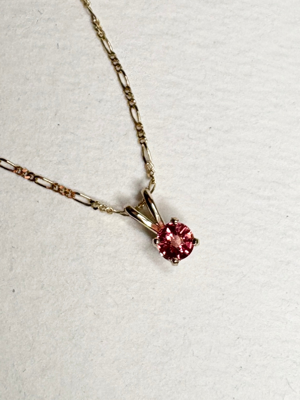A small, round pink sapphire pendant hangs from a delicate gold chain.