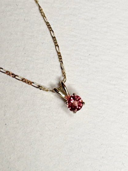 A small, round pink sapphire pendant hangs from a delicate gold chain.