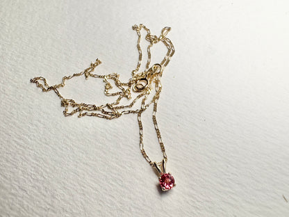 A delicate 14k gold chain holds a small, round pink sapphire pendant.