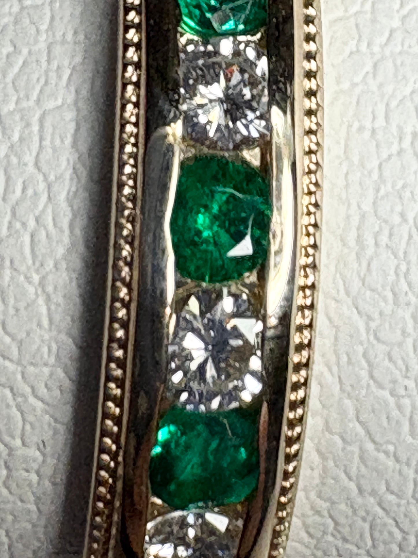 18k gold band ring with alternating emeralds and diamonds, featuring milgrain detail.