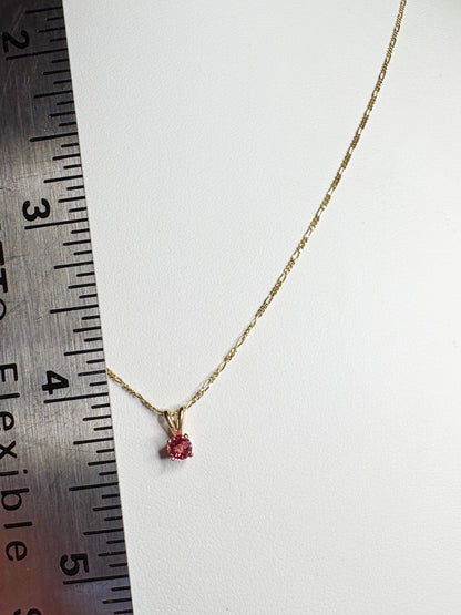 A delicate 14k gold necklace with a small pink sapphire pendant.