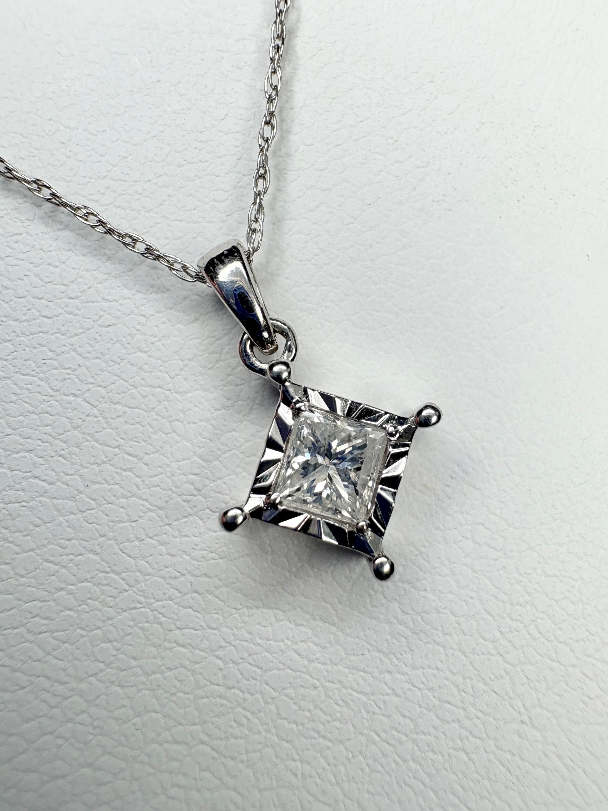 A princess cut diamond pendant necklace on a thin white gold chain.