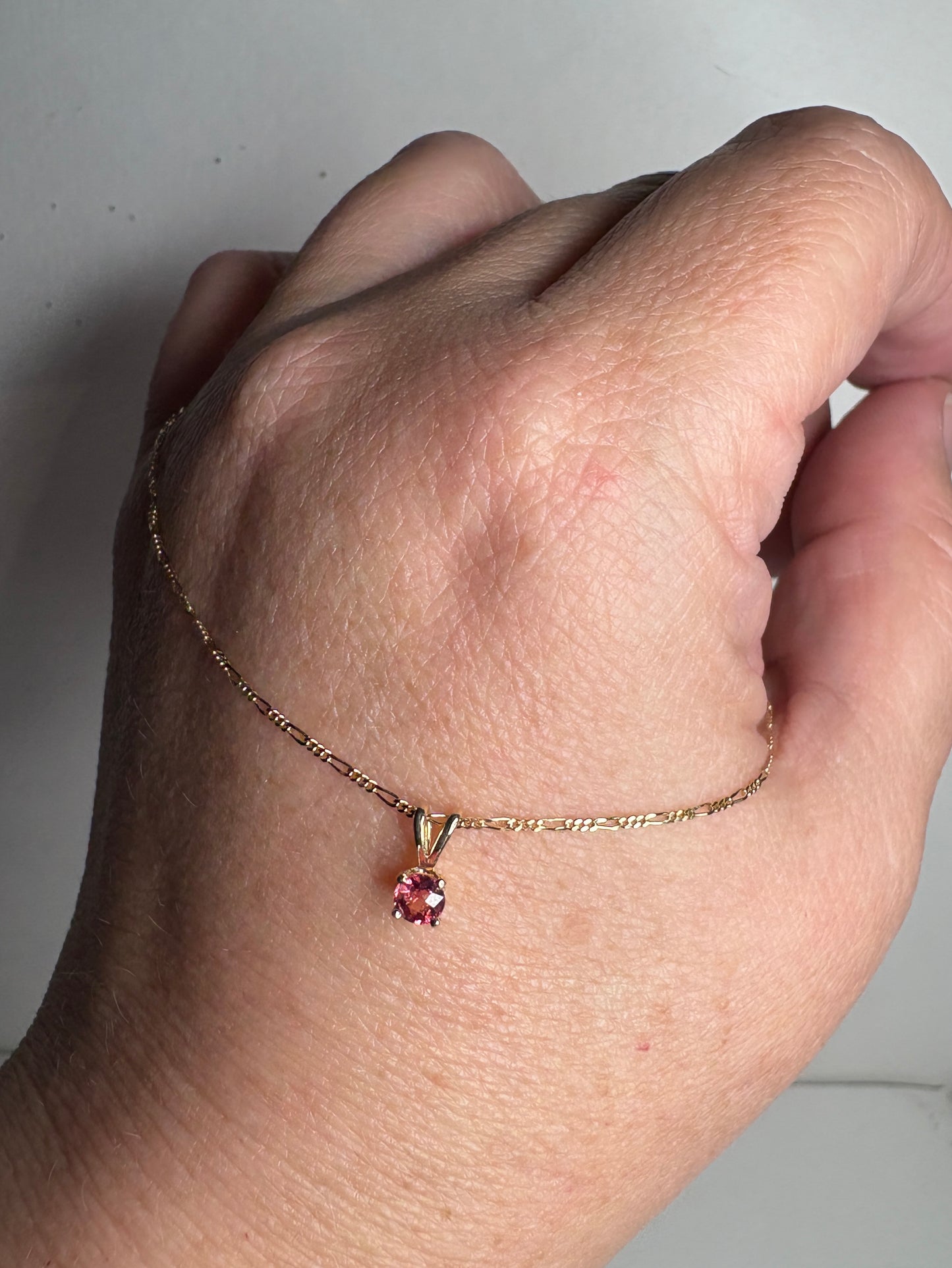 A delicate 14k gold chain holds a small, round pink sapphire pendant.