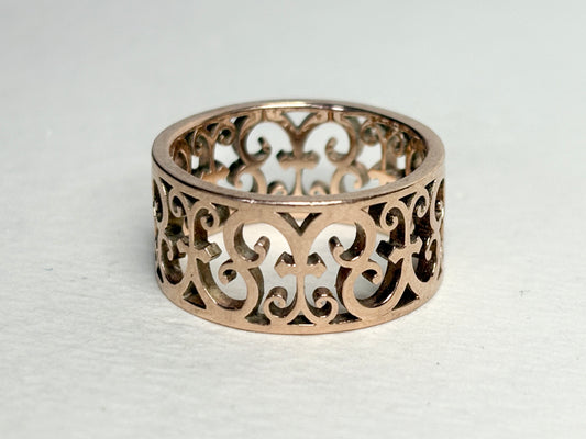 A rose gold colored Tiffany and Co. wide band ring with an intricate filigree design.