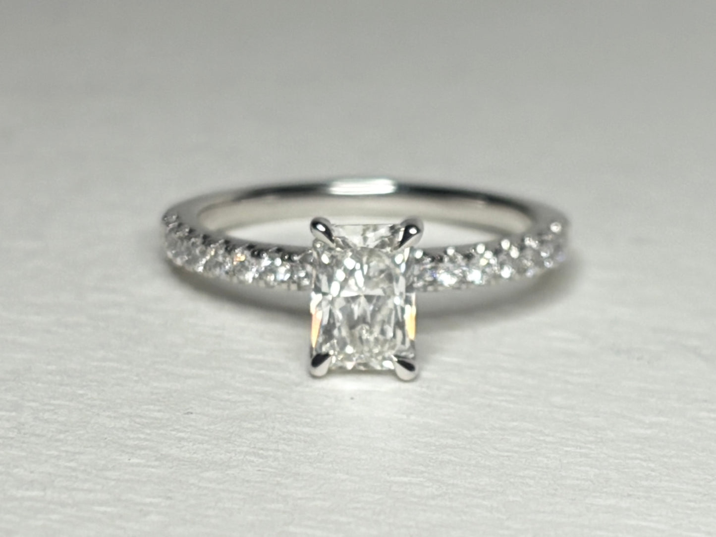 A 14k white gold engagement ring with a radiant cut diamond and pave band.