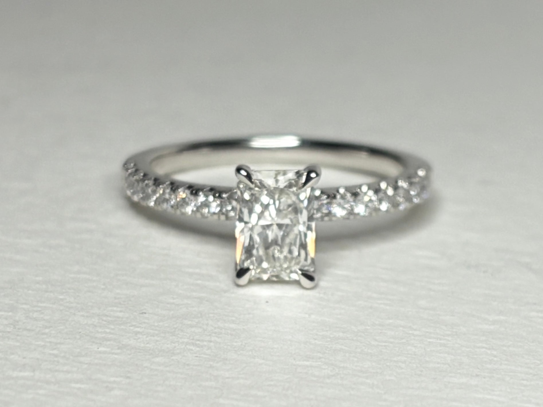 A 14k white gold engagement ring with a radiant cut diamond and pave band.
