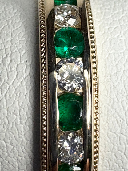 A channel-set band ring with alternating diamonds and emeralds in 18k gold.