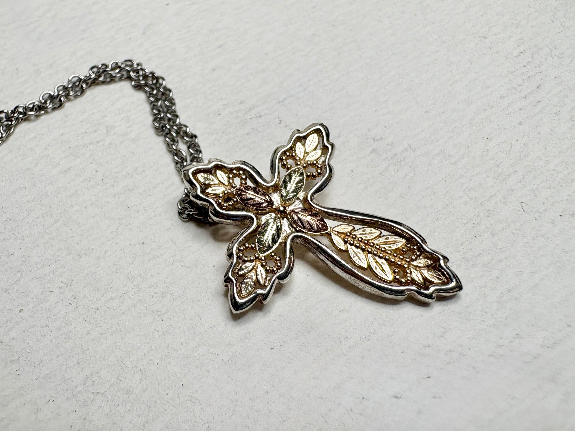 Black Hills Gold ornate cross pendant with sterling silver frame and stainless steel chain.