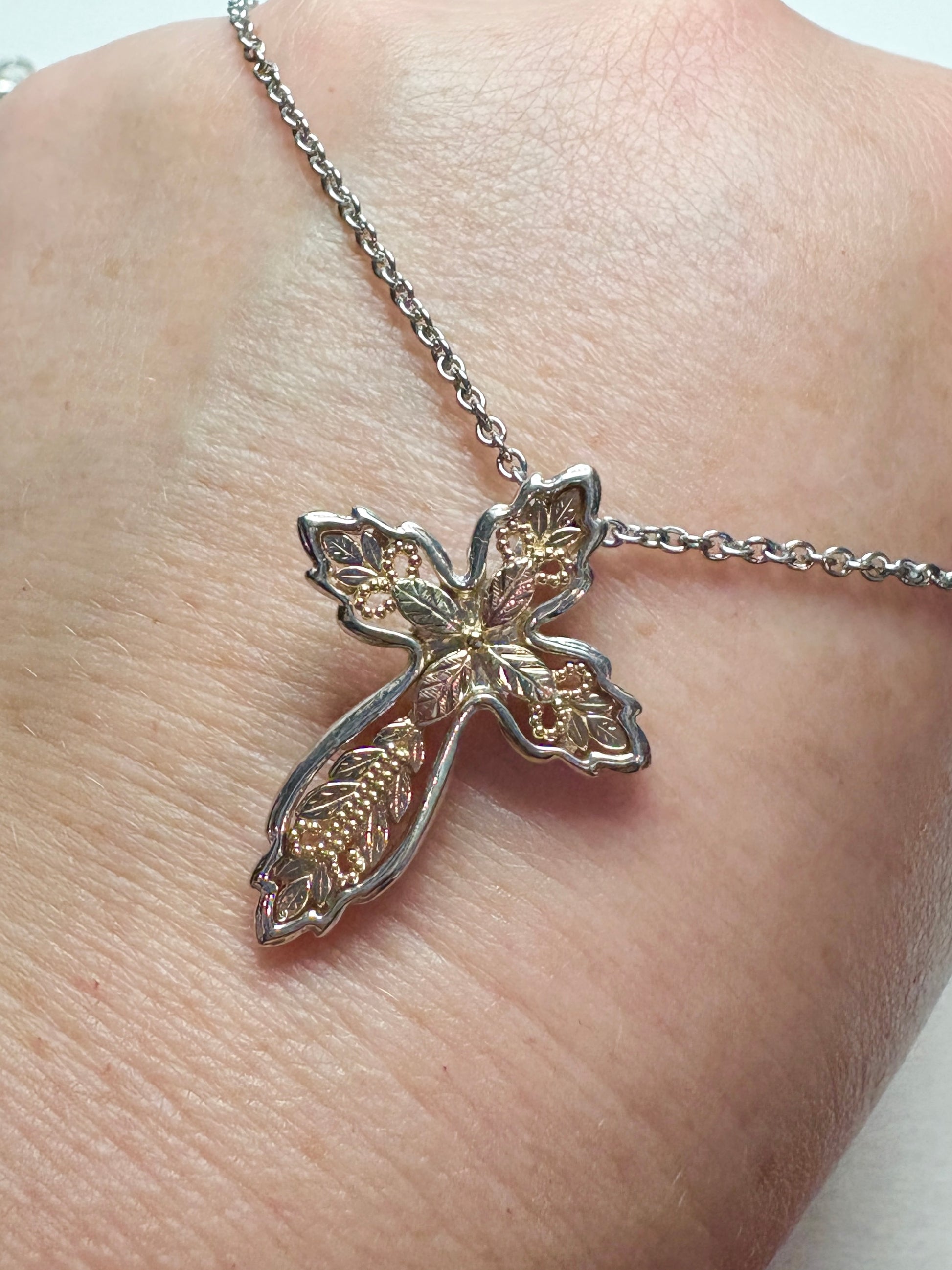 Black Hills Gold ornate cross pendant with green and rose gold leaves on a yellow gold base.