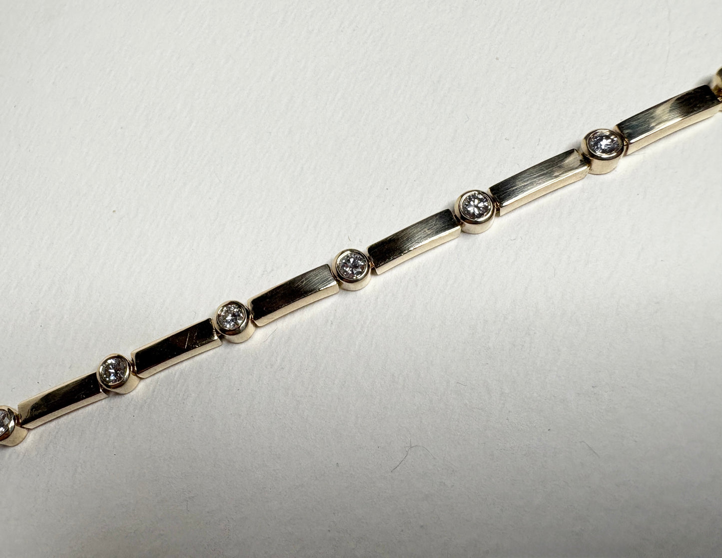 A 14k yellow gold tennis bracelet with 11 bezel-set diamonds.