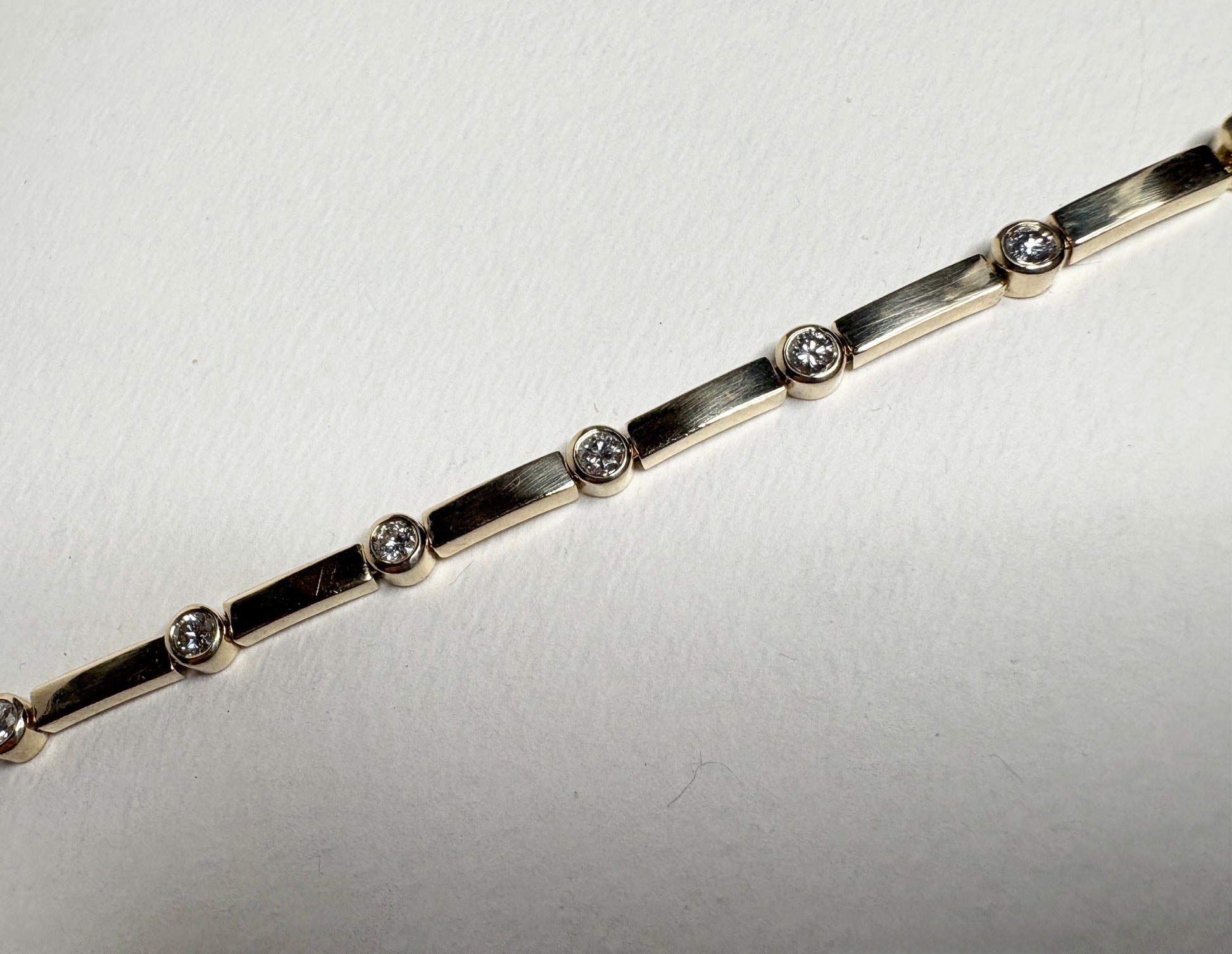 A 14k yellow gold tennis bracelet with 11 bezel-set diamonds.