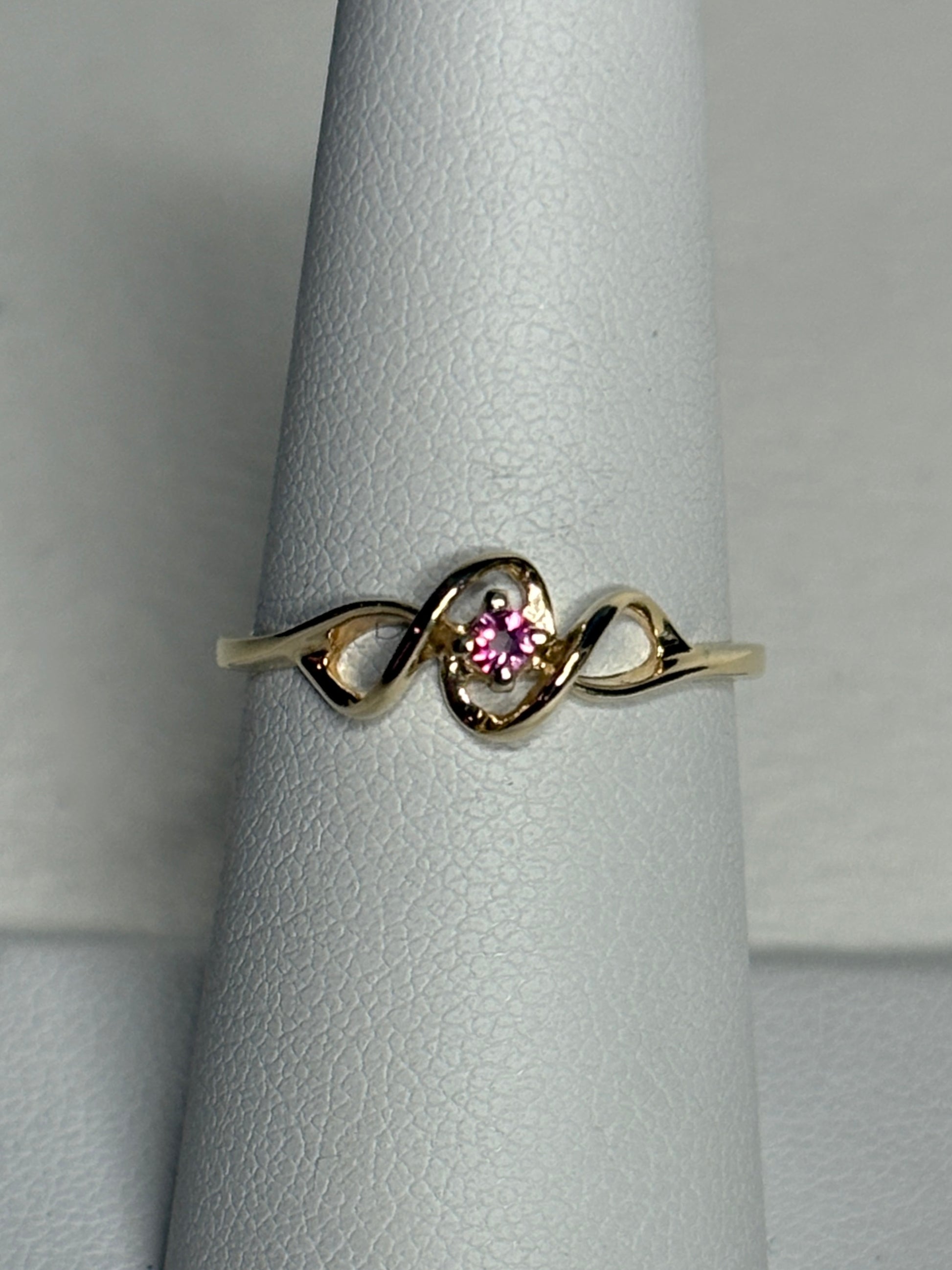 A delicate gold ring with a pink gemstone in a ribbon design.