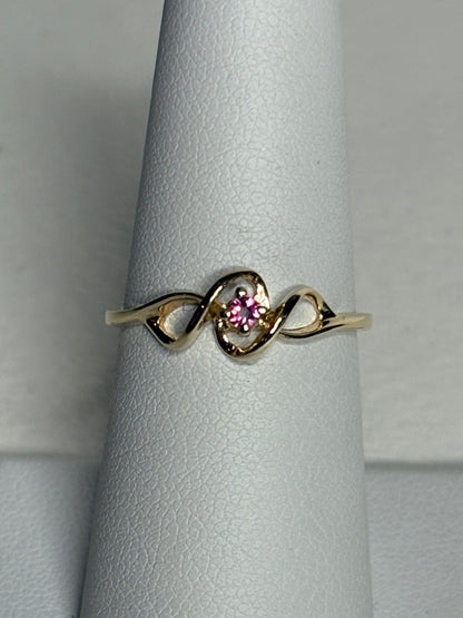 A delicate gold ring with a pink gemstone in a ribbon design.