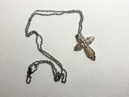 A Black Hills Gold ornate cross pendant with a sterling silver frame on a stainless steel chain.