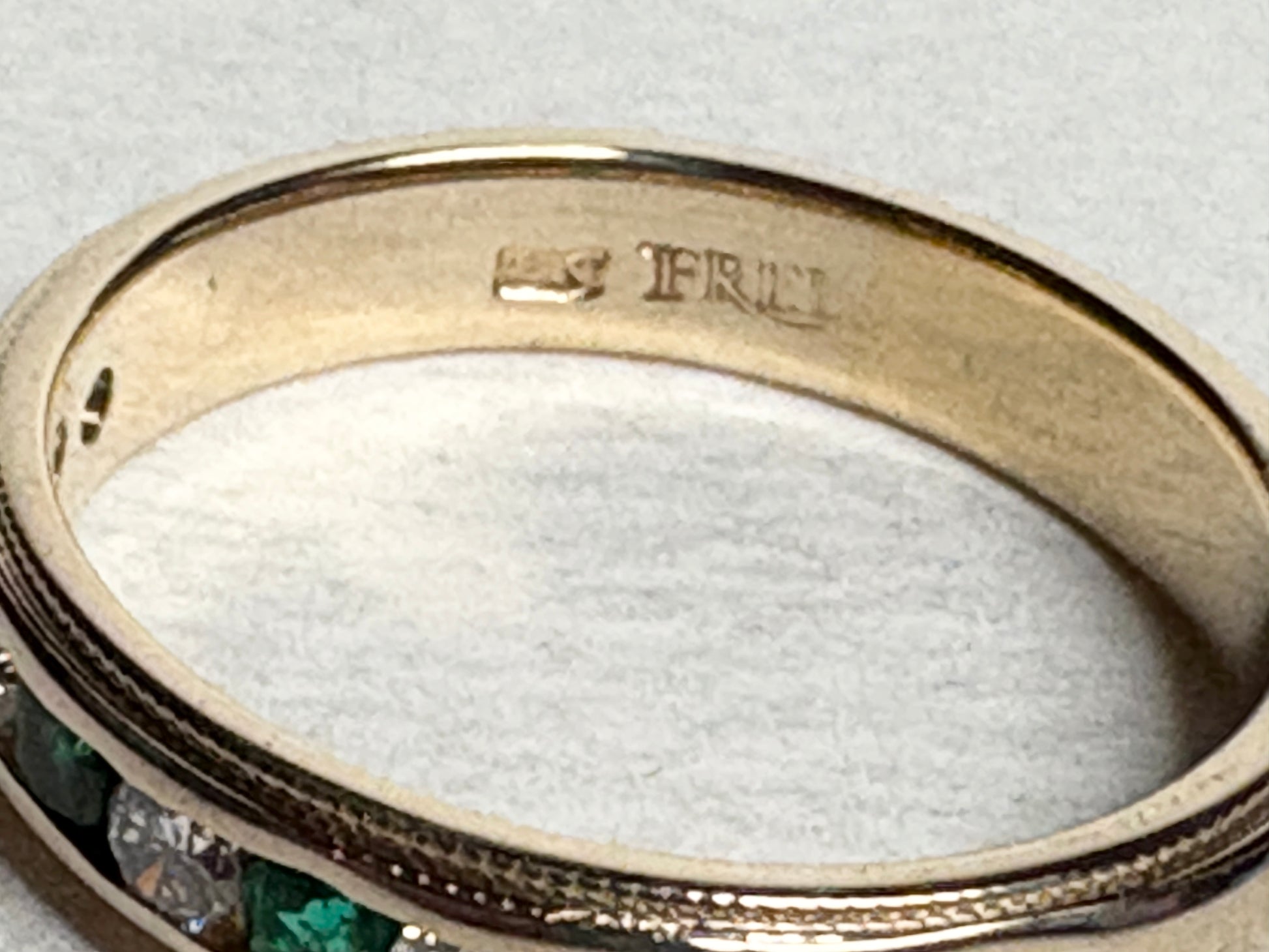 18k gold ring with channel-set diamonds and emeralds, featuring milgrain detailing.