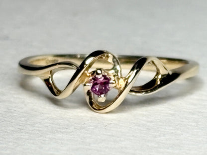 A 10k gold ribbon style ring with a pink bixbite gemstone.