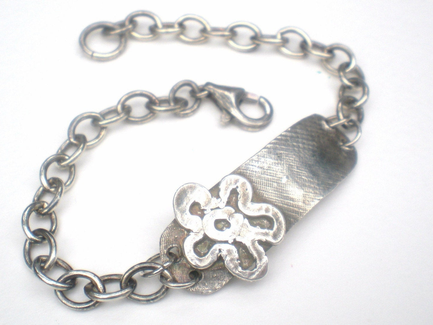 Sterling silver bracelet with a rugged ID tag and flower charm.