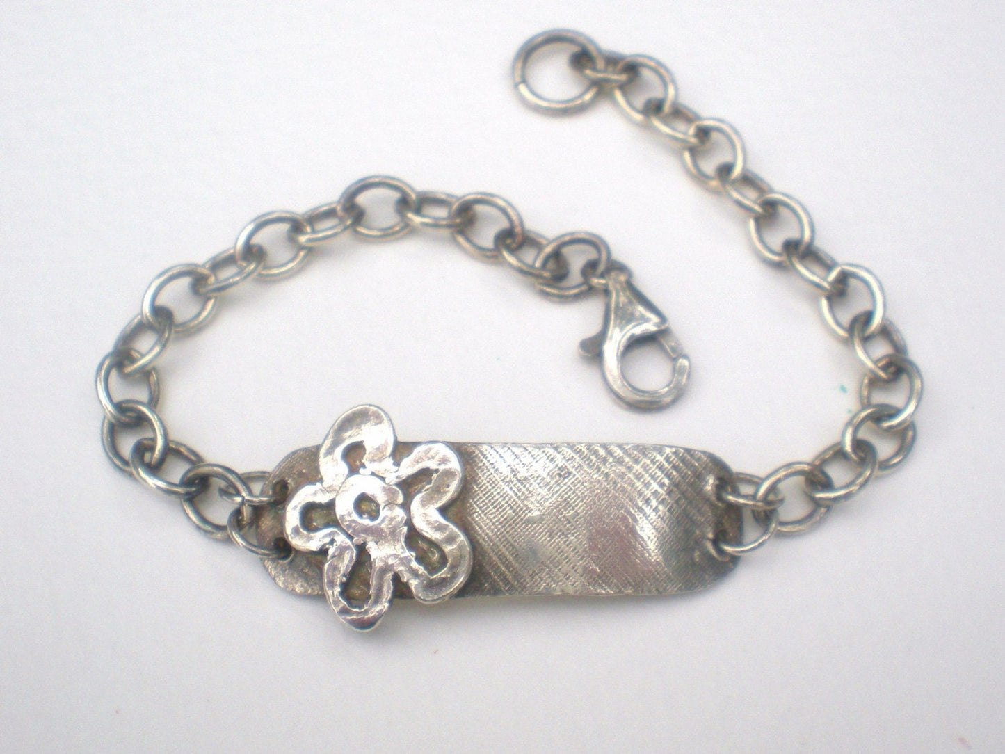 Sterling silver bracelet with a flower charm and rugged ID tag.