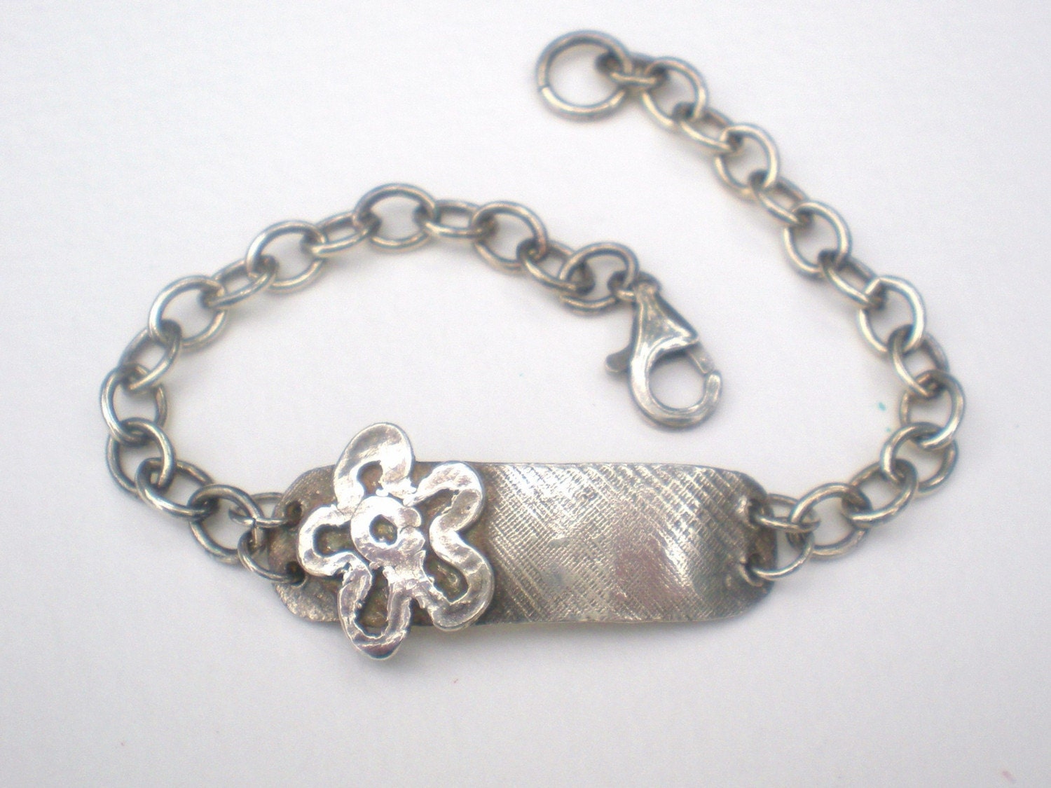 Sterling silver bracelet with a flower charm and rugged ID tag.