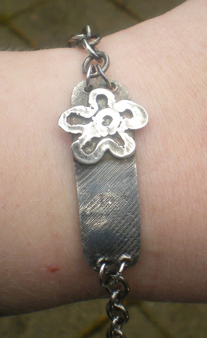Sterling silver bracelet with a flower charm and rugged texture.