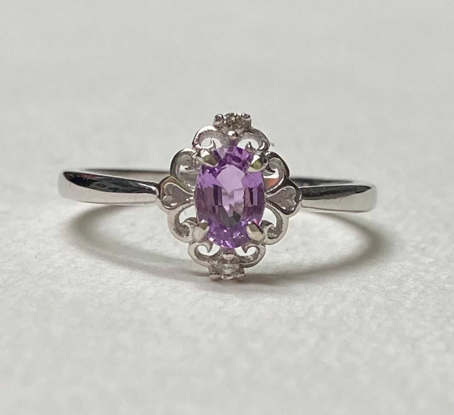 Sterling silver ring with oval pinkish-purple sapphire and diamond accents.